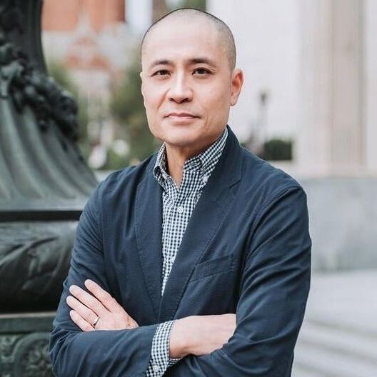 A man in a suit is standing with his arms crossed in front of a statue.