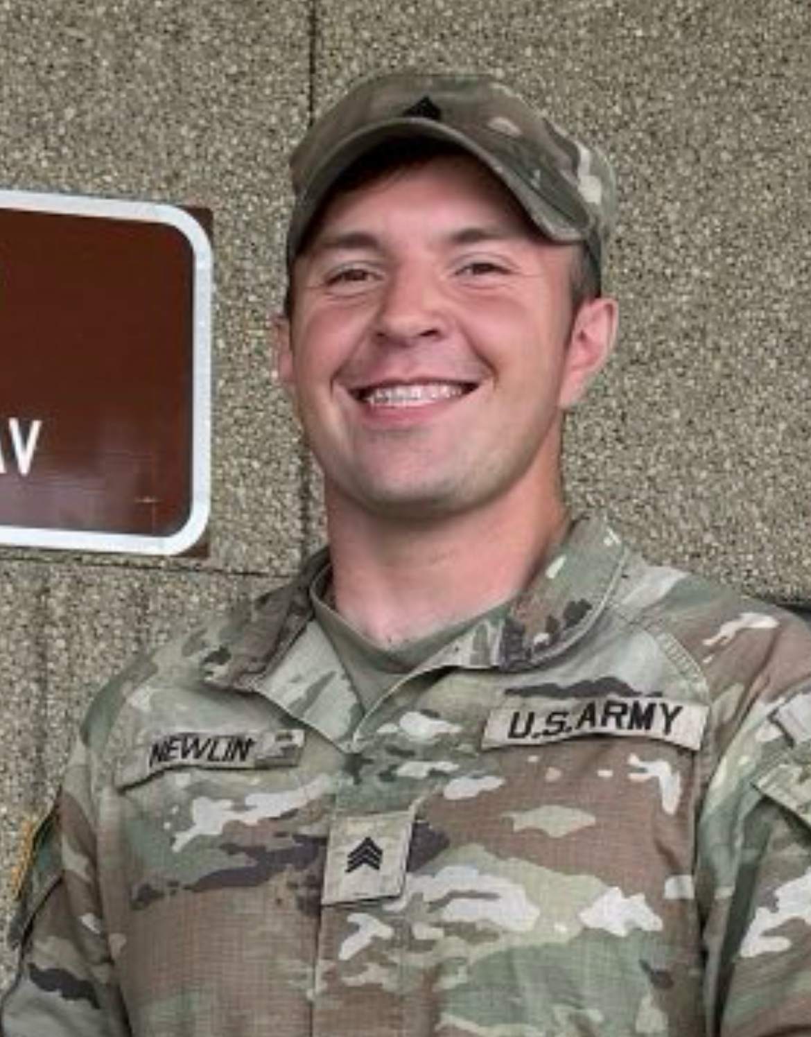 A man in a red shirt is standing in front of a bush.