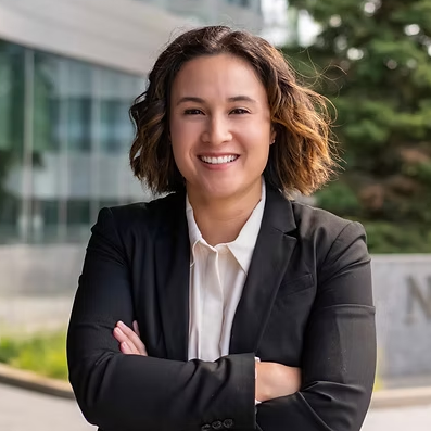 A woman in a suit and white shirt is smiling with her arms crossed.
