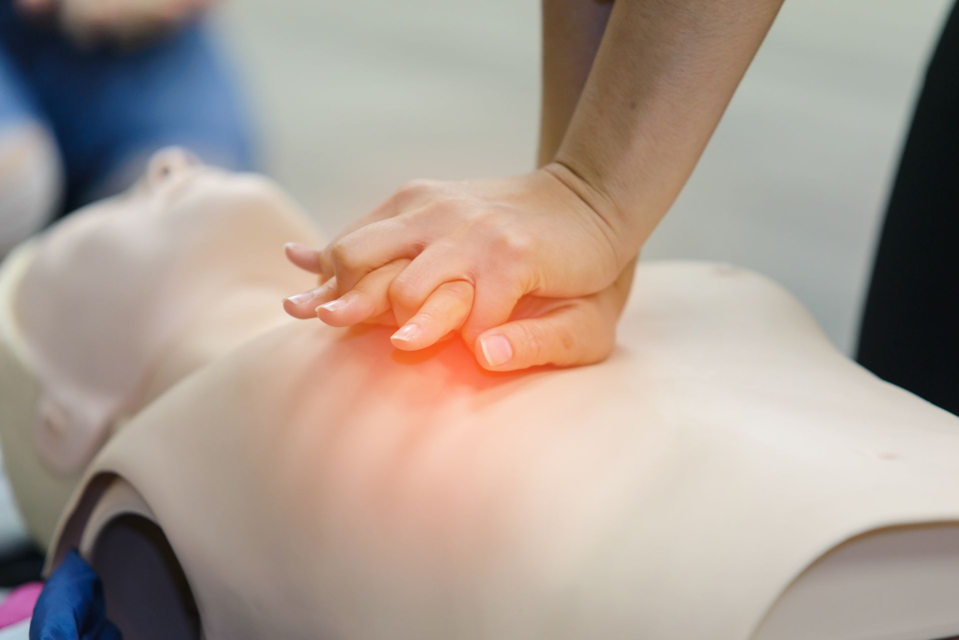 Close view of the hands of someone training CPR on a training dummy on the floor.