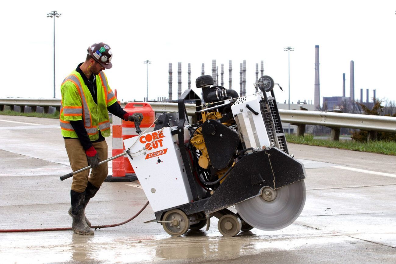 A man is using a concrete saw on a highway.