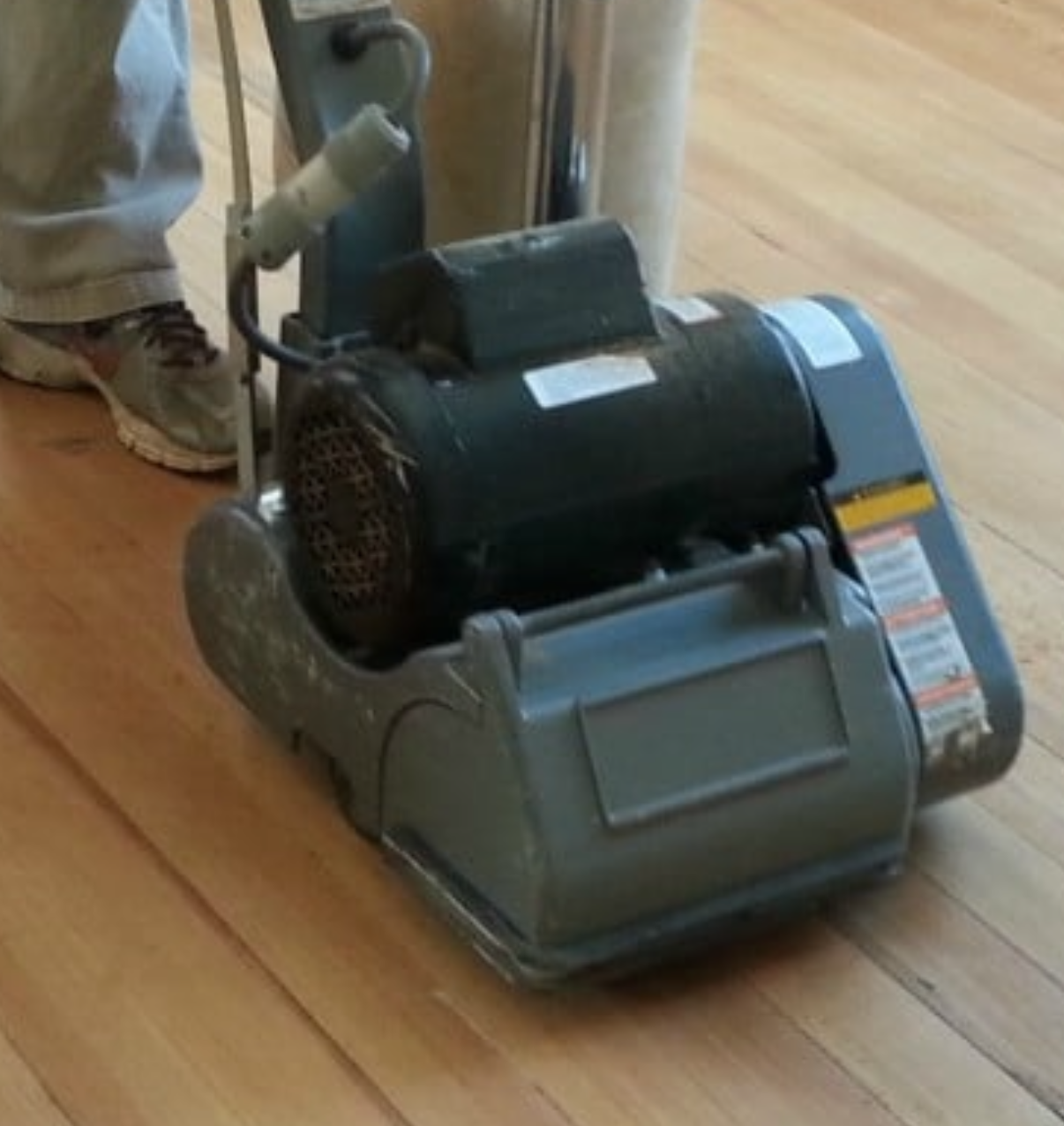 A person is using a machine to sand a wooden floor