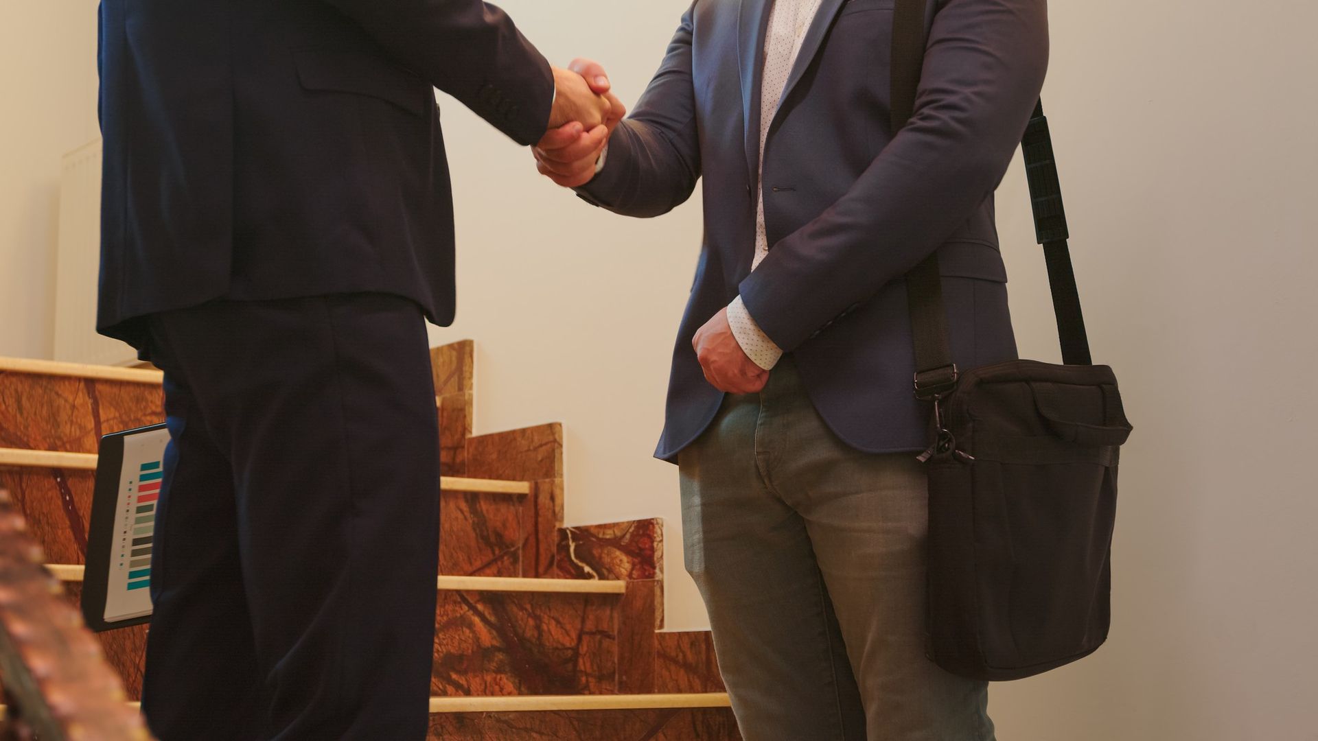 Two people in business attire shaking hands over a desk with a gavel and papers, suggesting a legal agreement