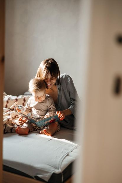 Adult and child reading together on a bed in warm sunlight