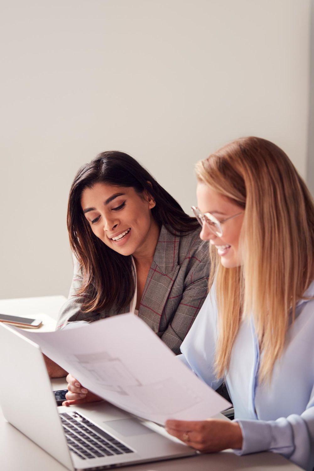 Two coworkers reviewing printed documents beside a laptop in a bright office setting