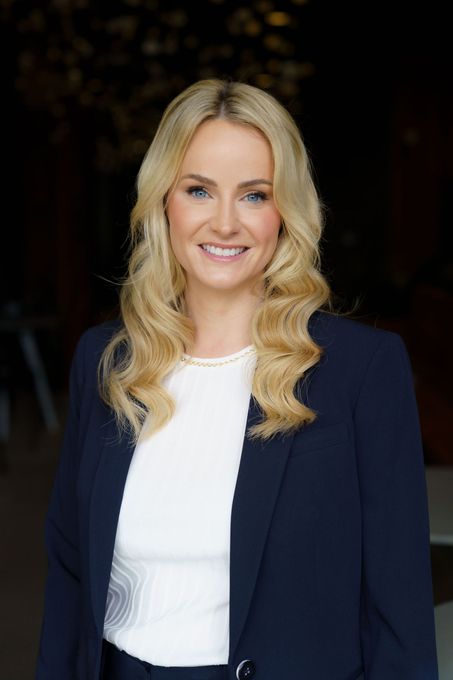 Portrait of a smiling woman in a navy blazer and white top against a dark background