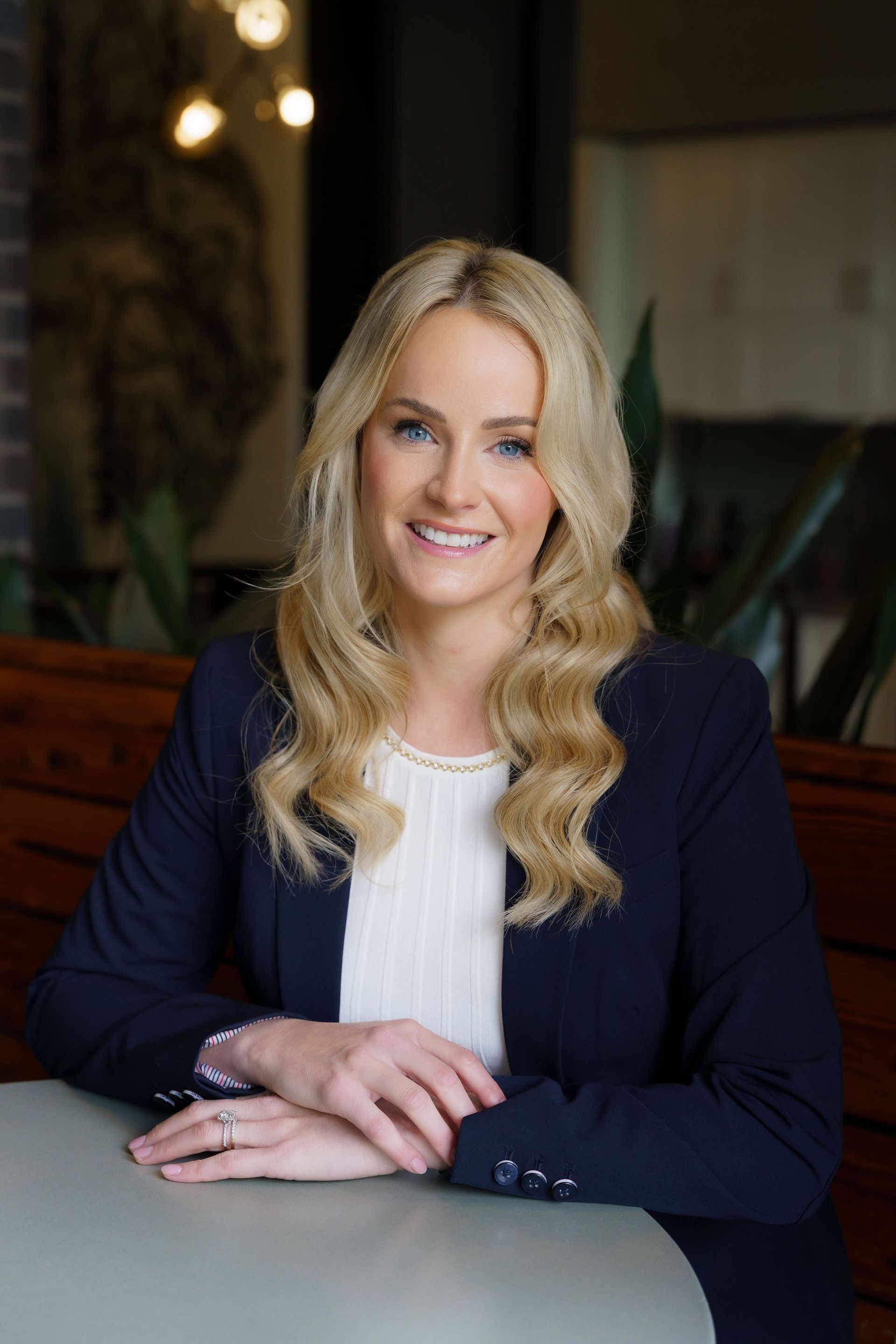 Portrait of a smiling woman in a navy blazer seated at a table indoors