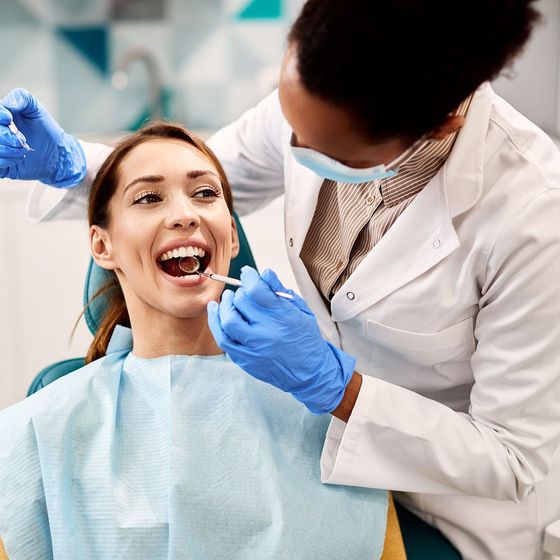 Dentist examining a smiling patient’s teeth with blue gloves in a dental clinic Dentist examining a smiling patient’s teeth with blue gloves in a dental clinic