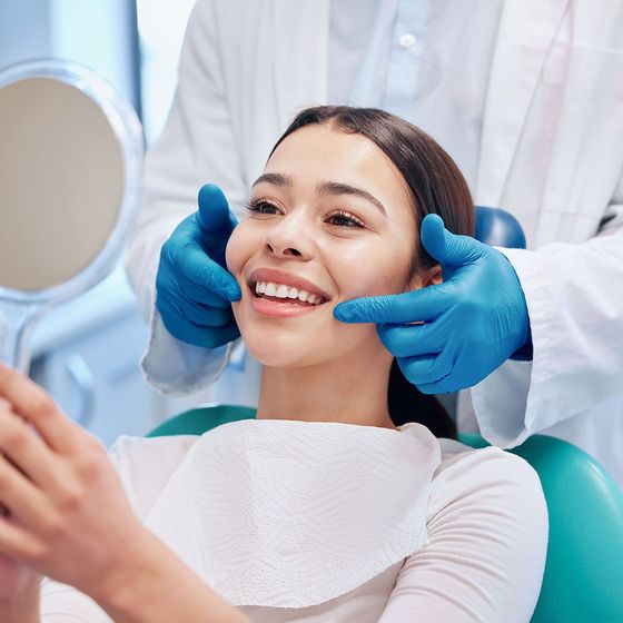 Patient smiling in a dental chair while a dentist examines her teeth with blue gloves Patient smiling in a dental chair while a dentist examines her teeth with blue gloves