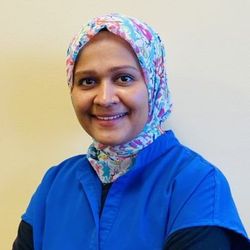 Smiling person in a blue shirt and floral headscarf against a plain light background Smiling person in a blue shirt and floral headscarf against a plain light background
