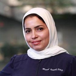 Portrait of a smiling person in a white headscarf and dark purple top against a blurred background Portrait of a smiling person in a white headscarf and dark purple top against a blurred background