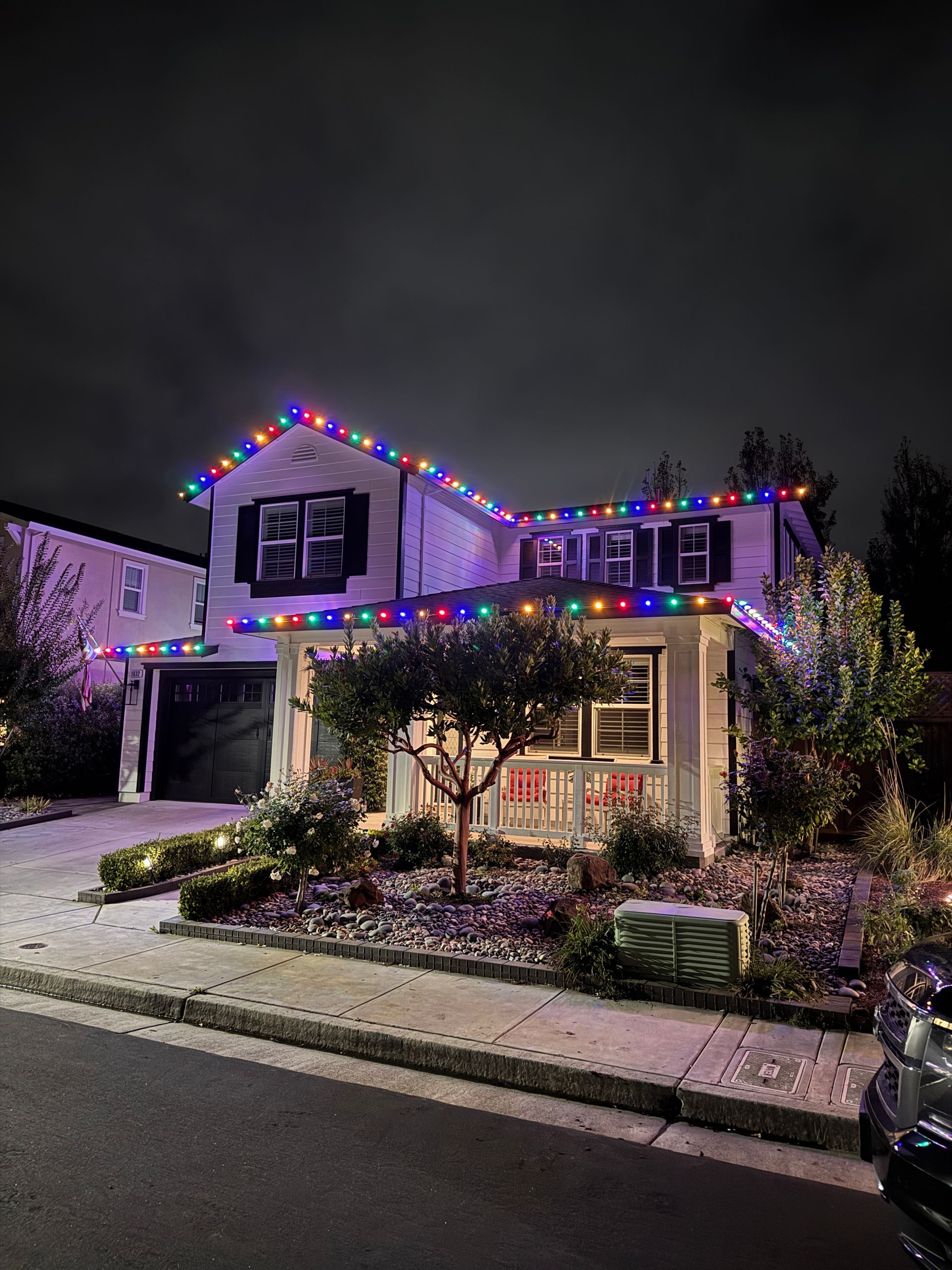 Two-story house at night decorated with colorful Christmas lights and snow on the front lawn.