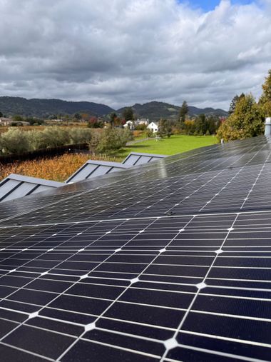Solar panels on a rooftop beside fields and hills under a cloudy sky.