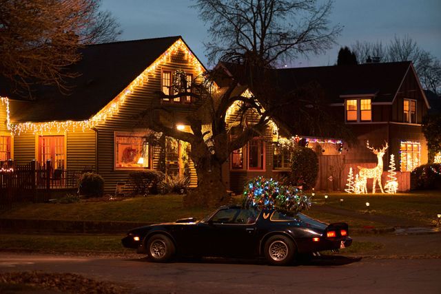 Car in front of a house lit with Christmas lights at night