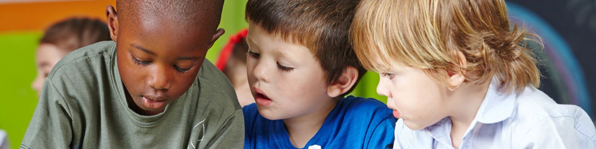 Three young boys are looking at something together in a classroom.