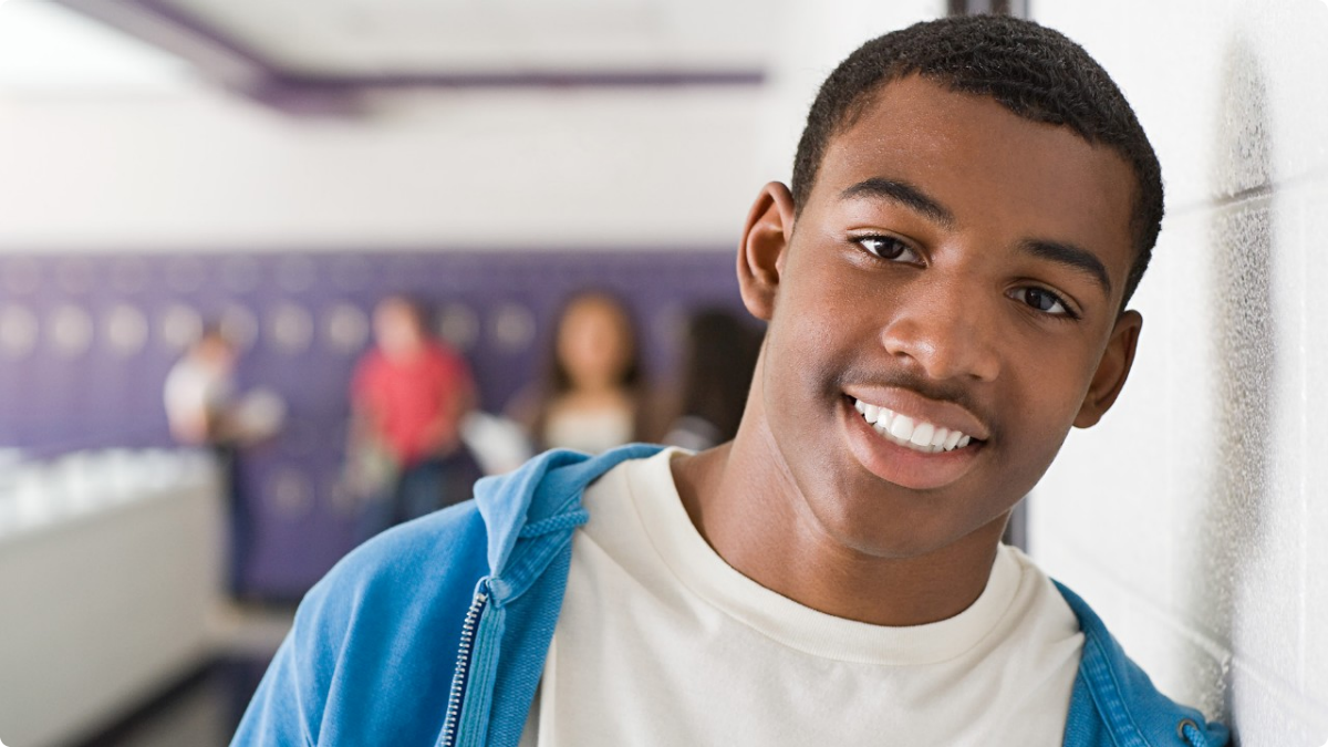 A young man is leaning against a wall and smiling