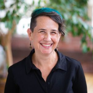 a woman wearing a black shirt and earrings is smiling for the camera .