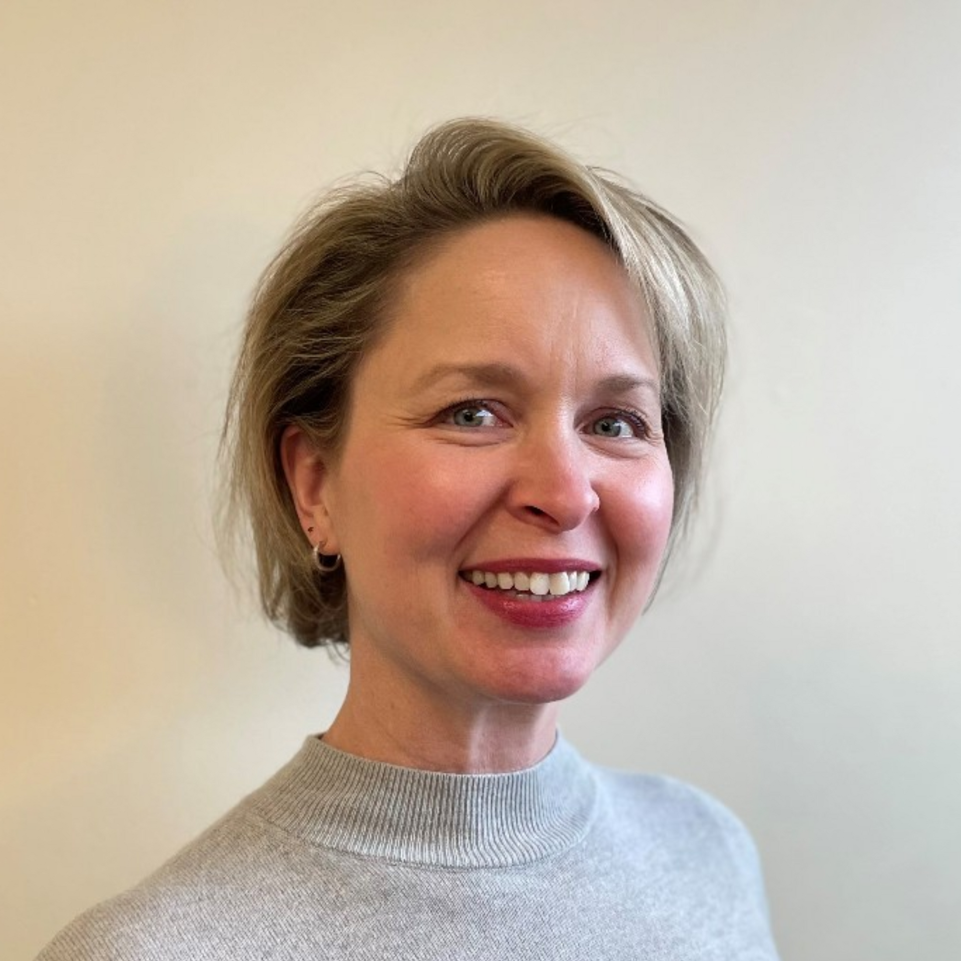a woman in a grey sweater is smiling for the camera .