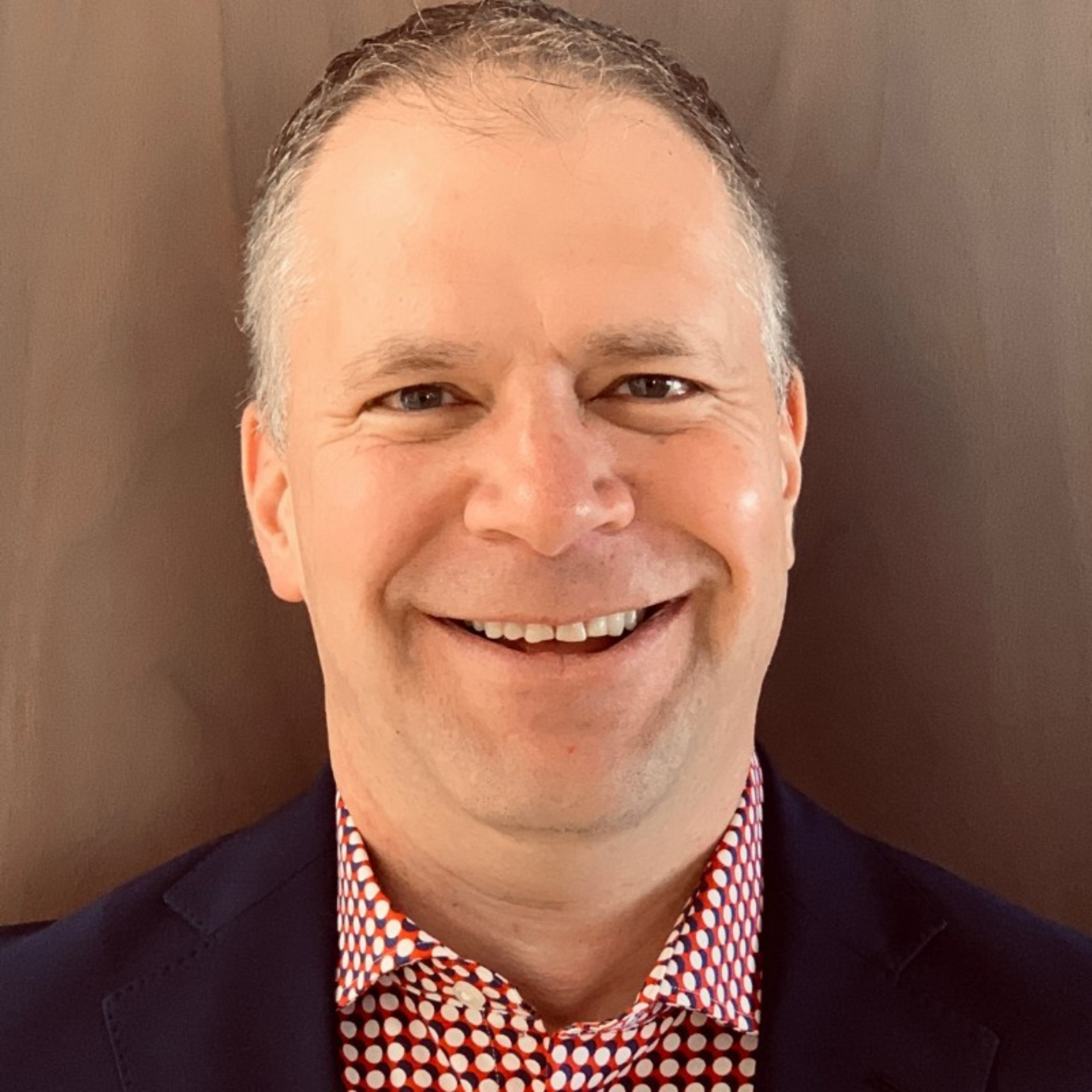 a man in a suit and polka dot shirt is smiling for the camera .