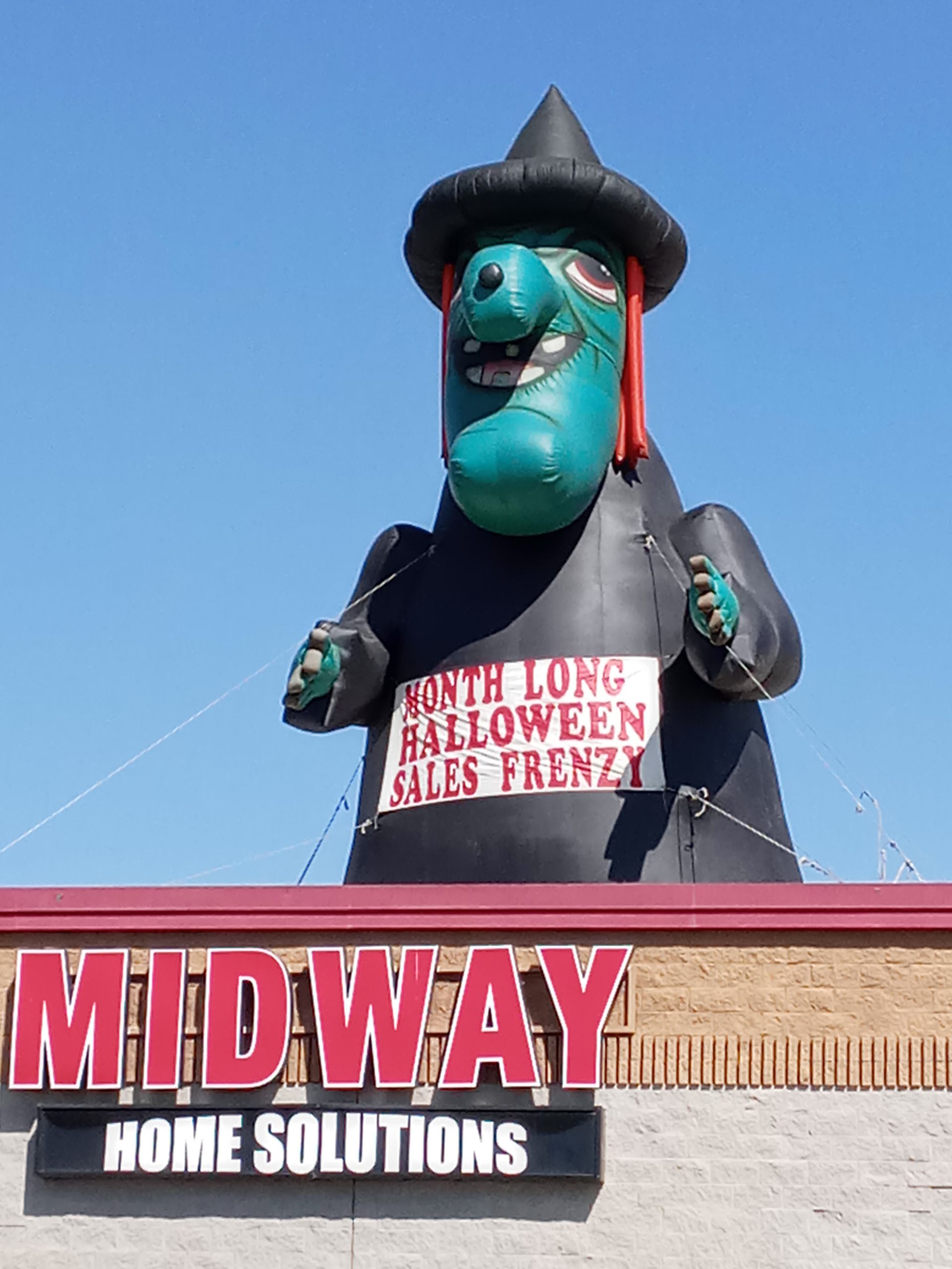 A midway home solutions sign with a giant inflatable witch on top