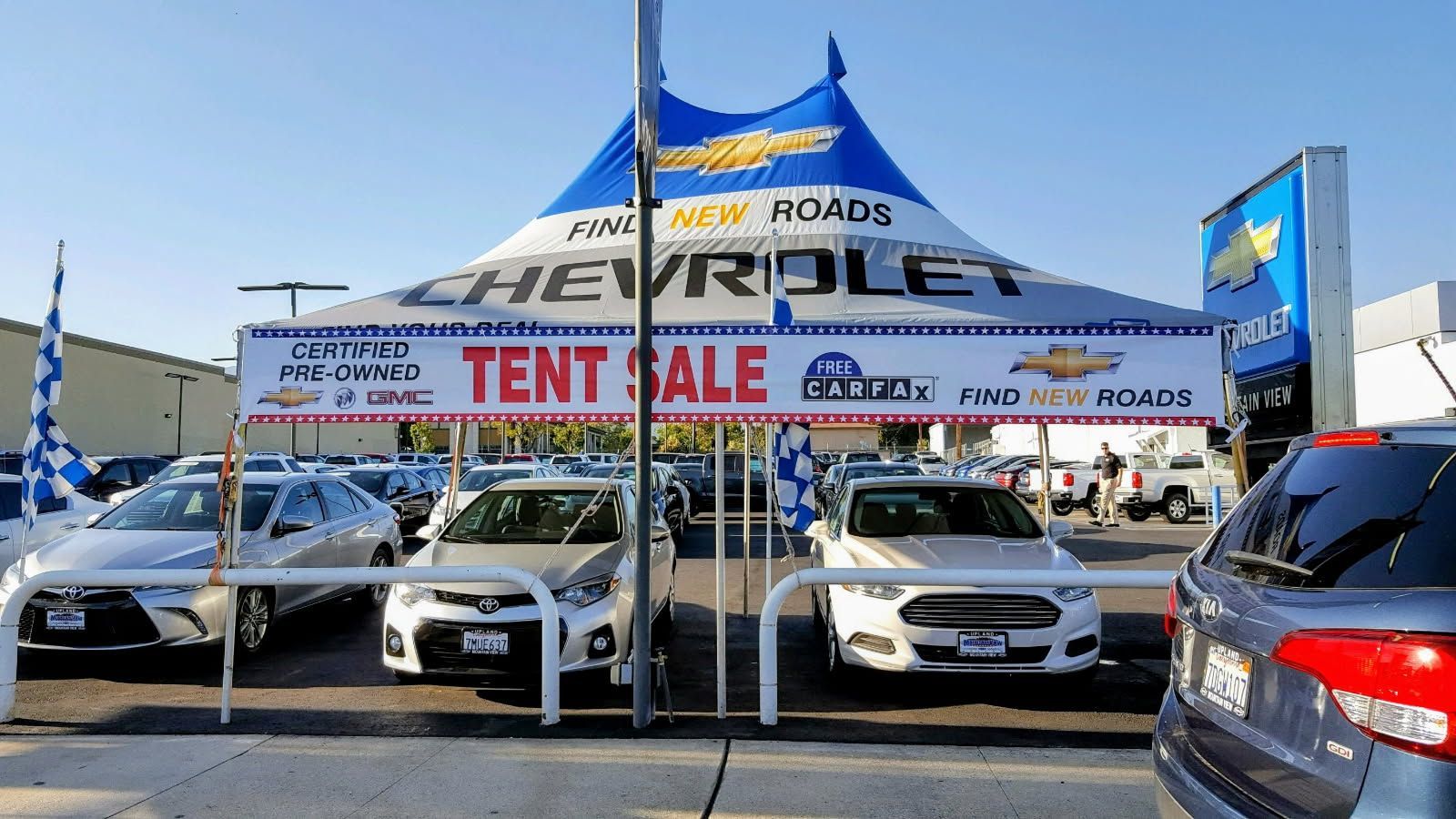 A chevrolet tent is sitting in front of a lot of cars.