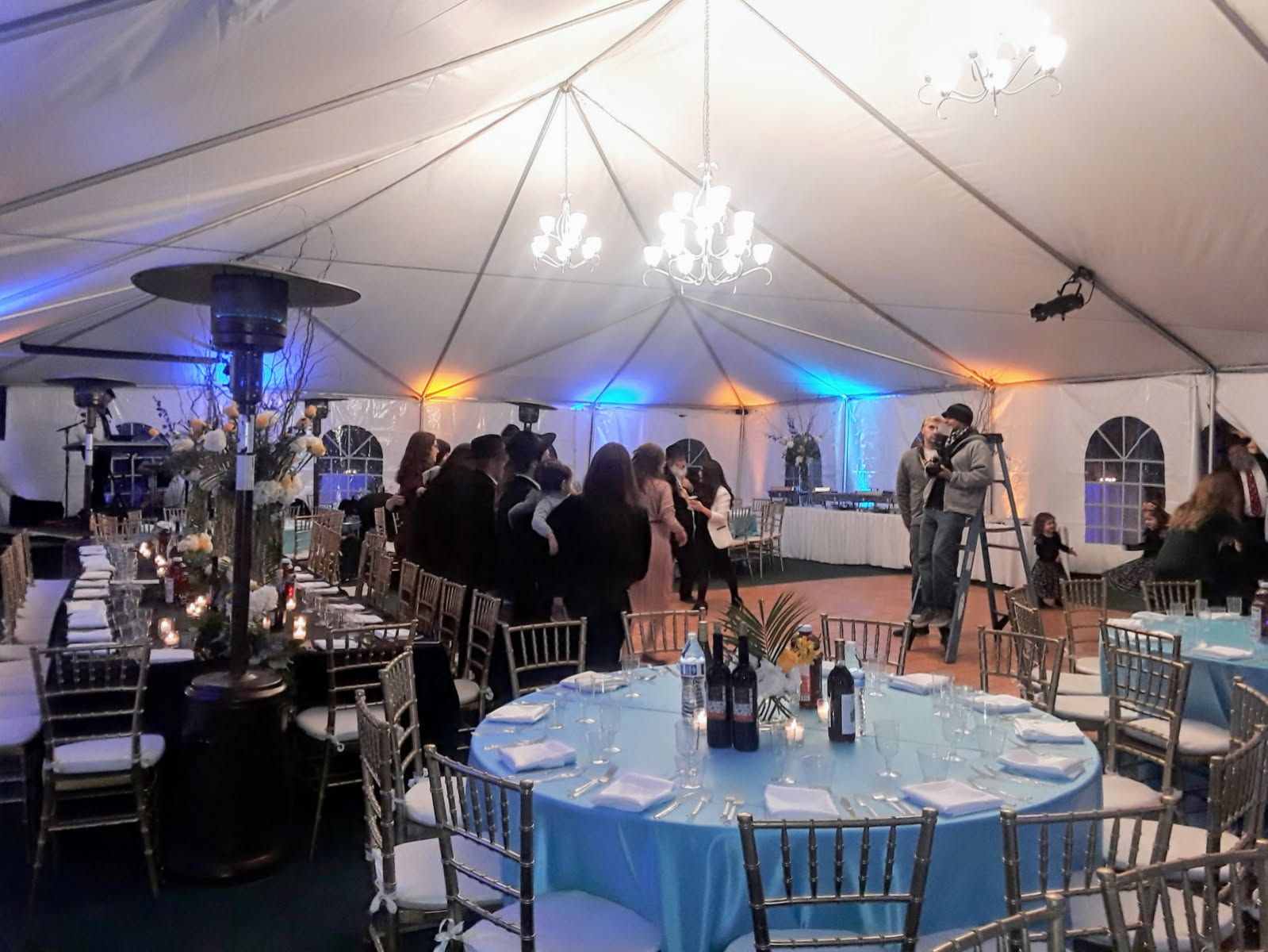 A group of people are dancing under a tent at a wedding reception.