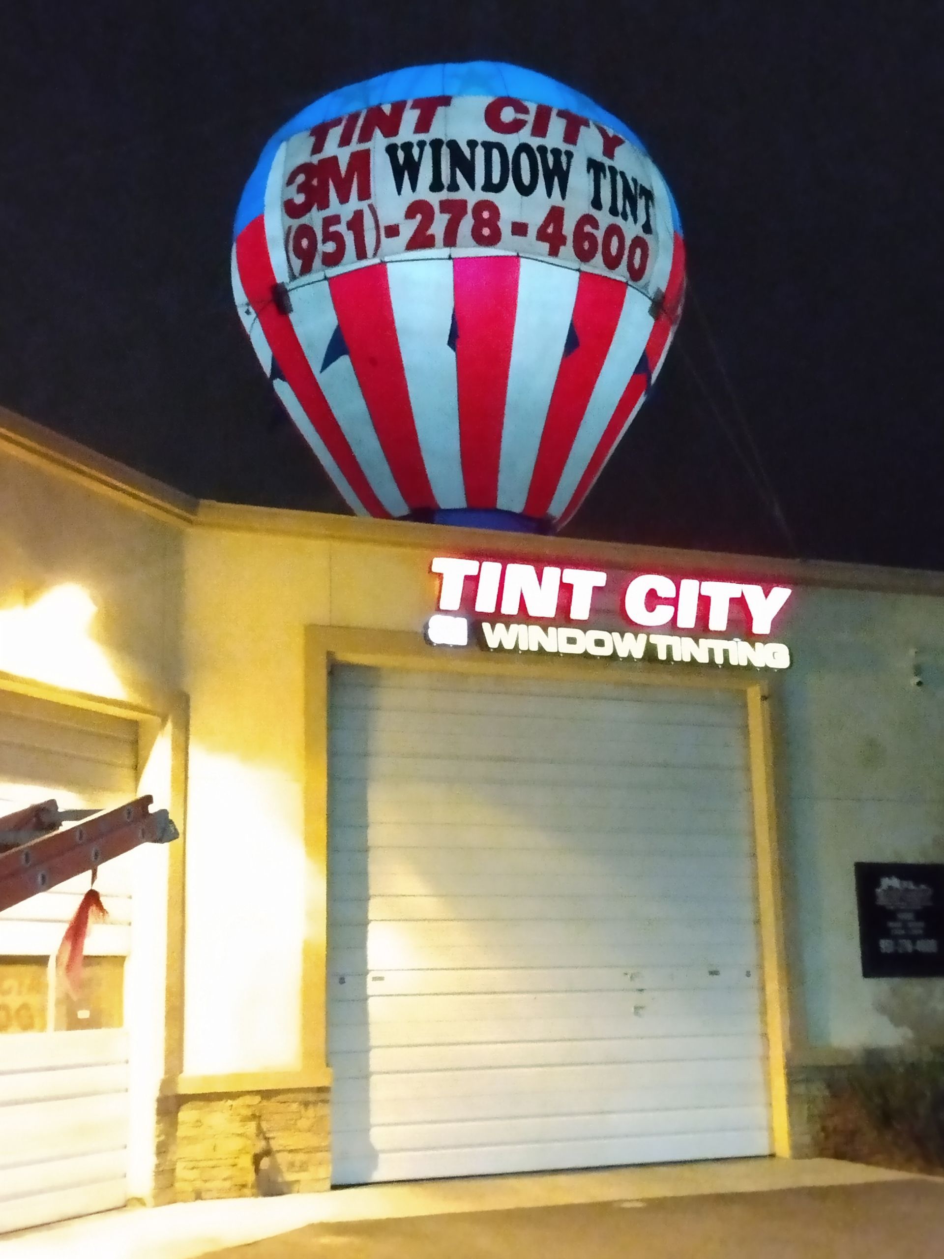 A red white and blue hot air balloon in front of a tint city window tinting store
