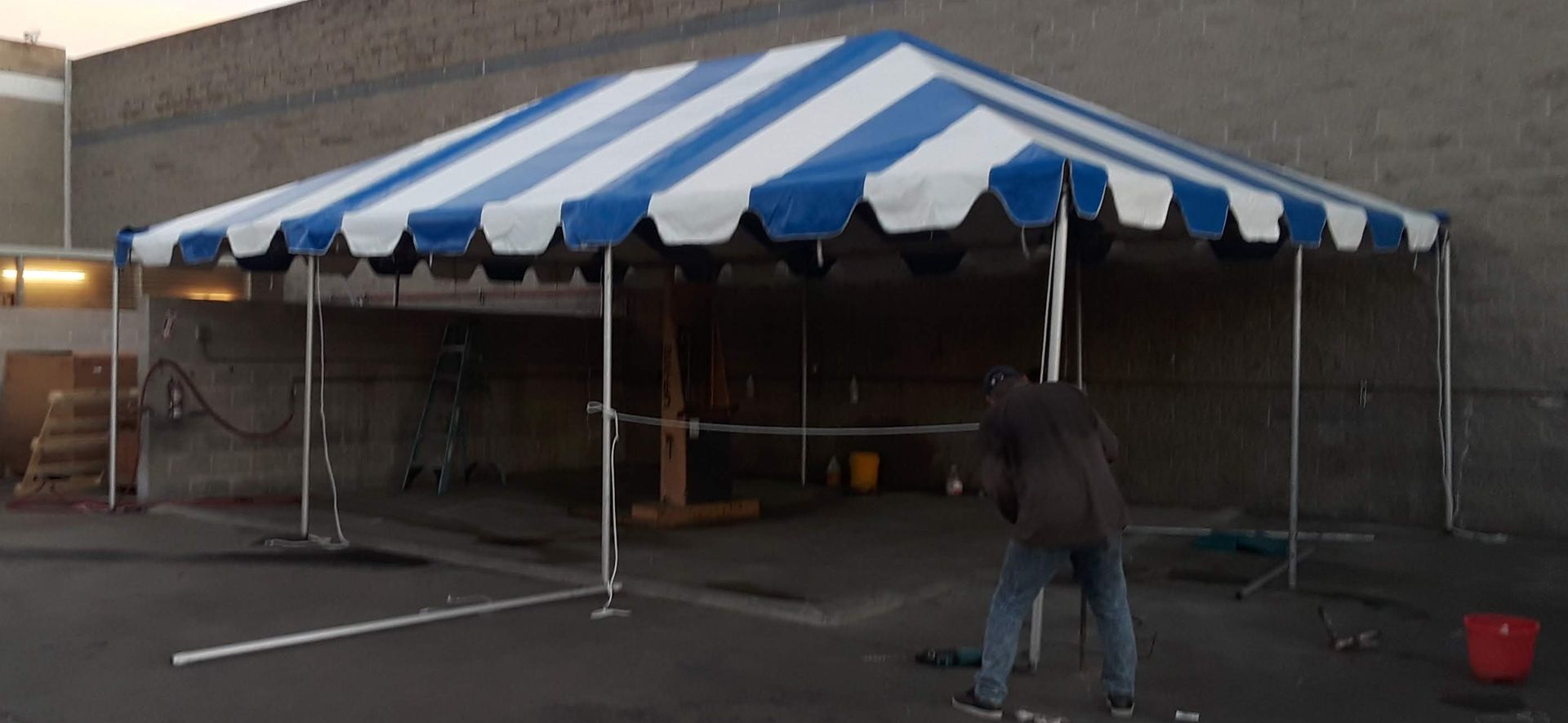 A man is standing under a blue and white striped tent.