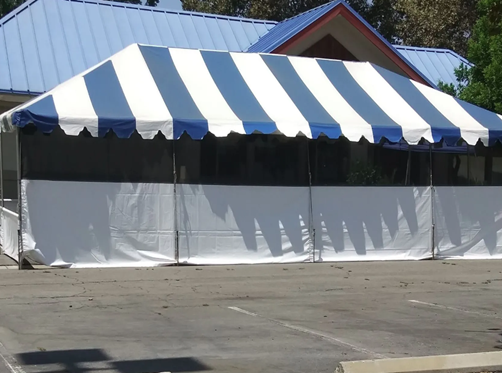 Blue and white striped tent with white side panels set up in a parking lot.