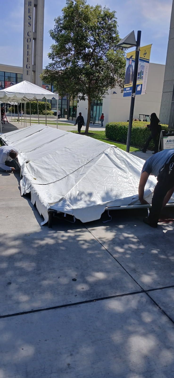A man is working on a large white tent on the sidewalk.