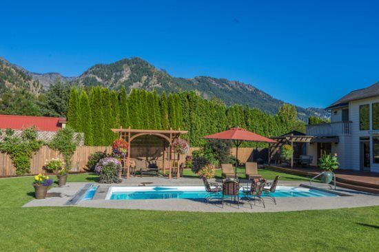 Backyard pool with patio chairs, gazebo, mountains, and a manicured lawn under a clear blue sky