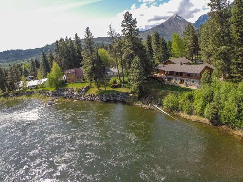Riverfront cabins and pine trees beside a mountain lake under a bright sky