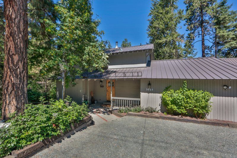 House with a metal roof, front porch, and driveway surrounded by tall pine trees.
