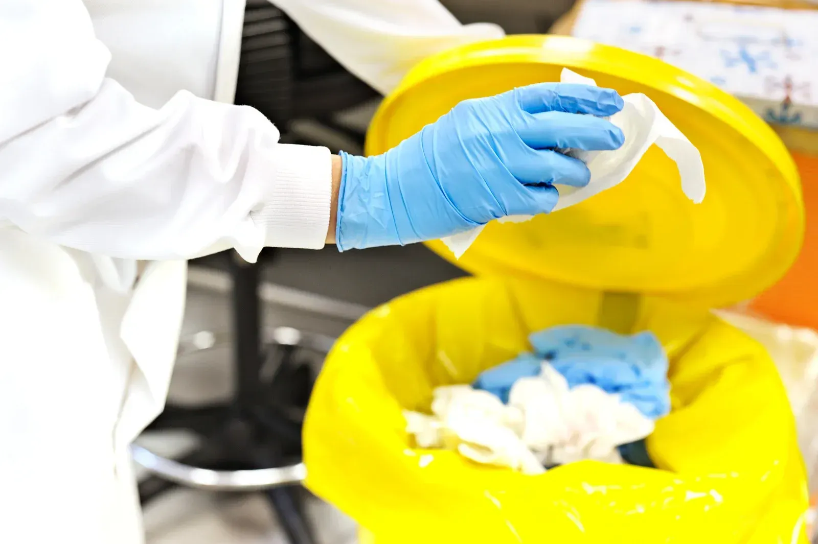 A person wearing blue gloves is cleaning a yellow trash can.
