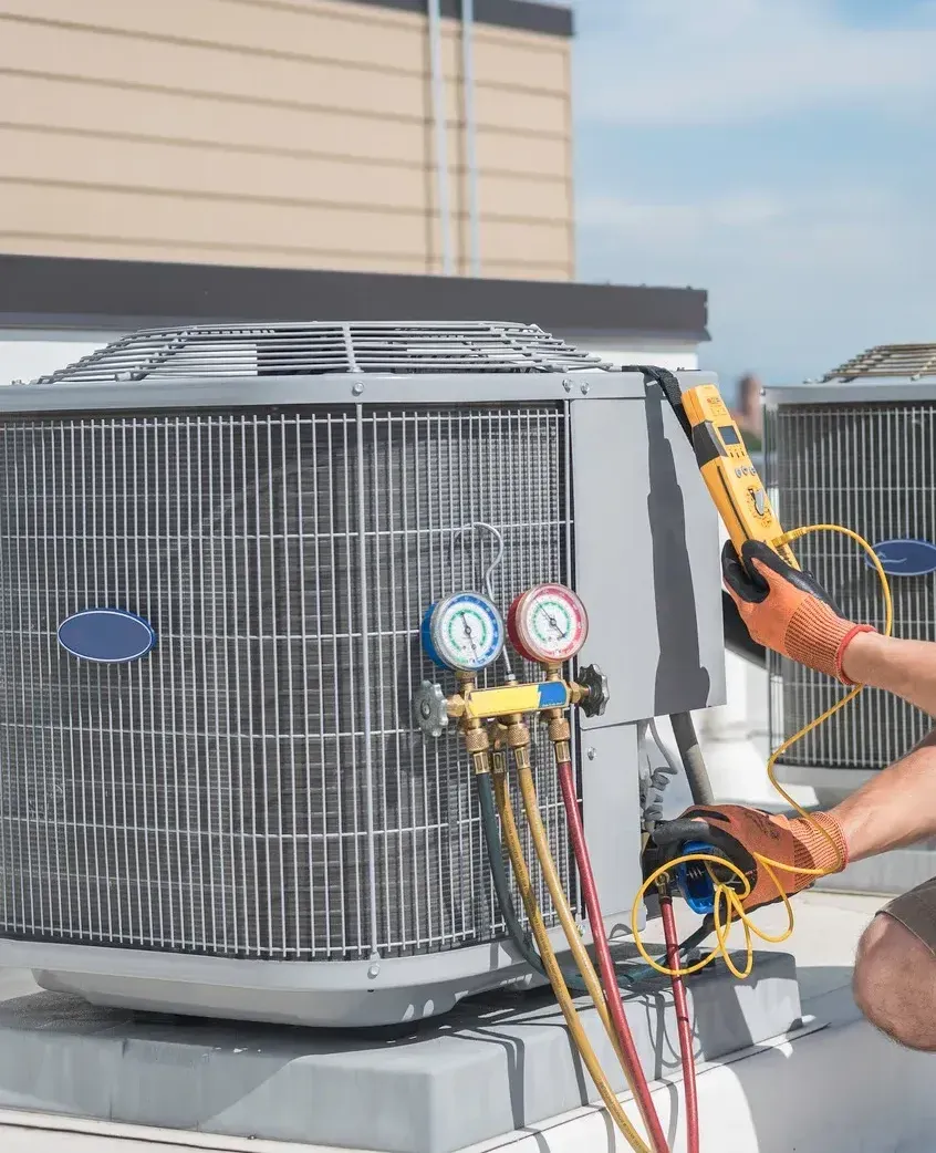 A man is working on an air conditioner on the roof of a building.