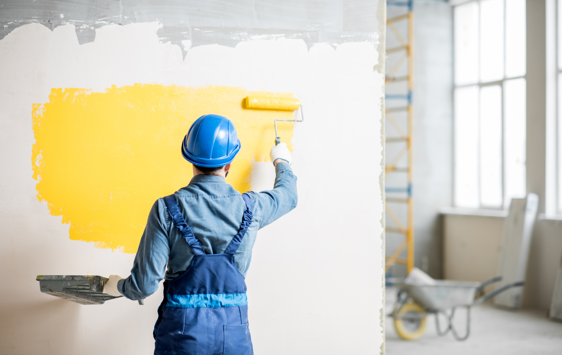 A man is painting a wall yellow with a roller.