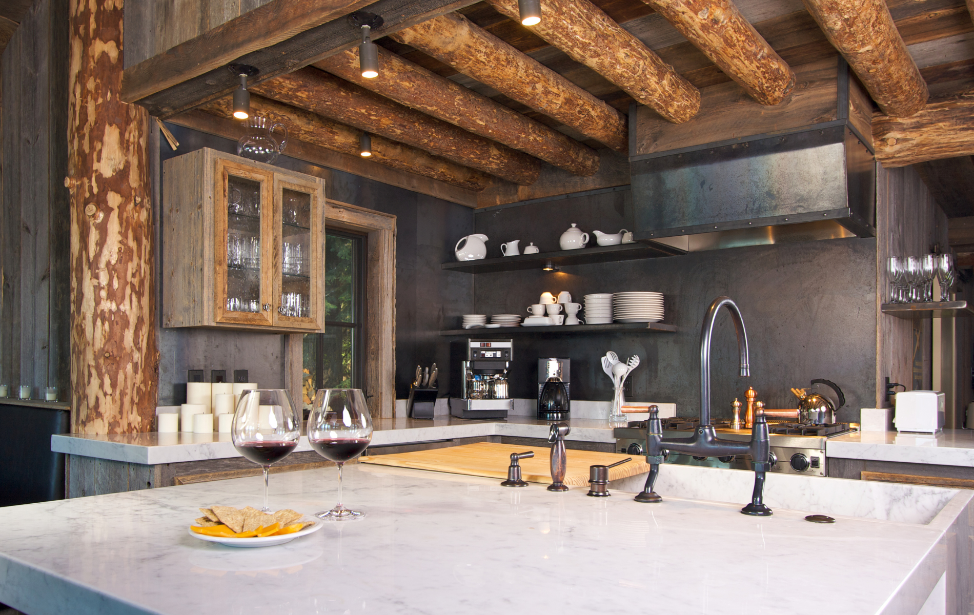 A kitchen with a stove , sink , and two glasses of wine on the counter.