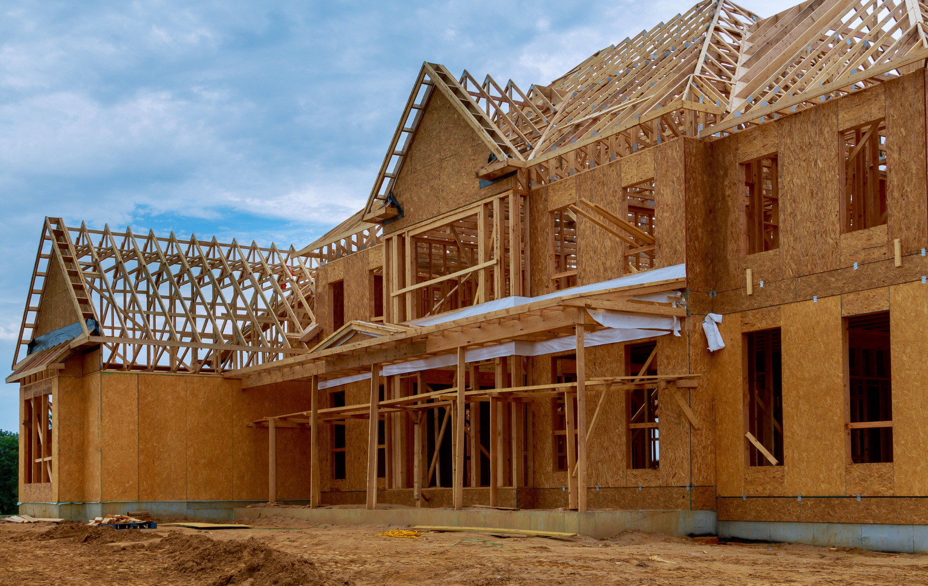 A large wooden house is being built in a dirt field