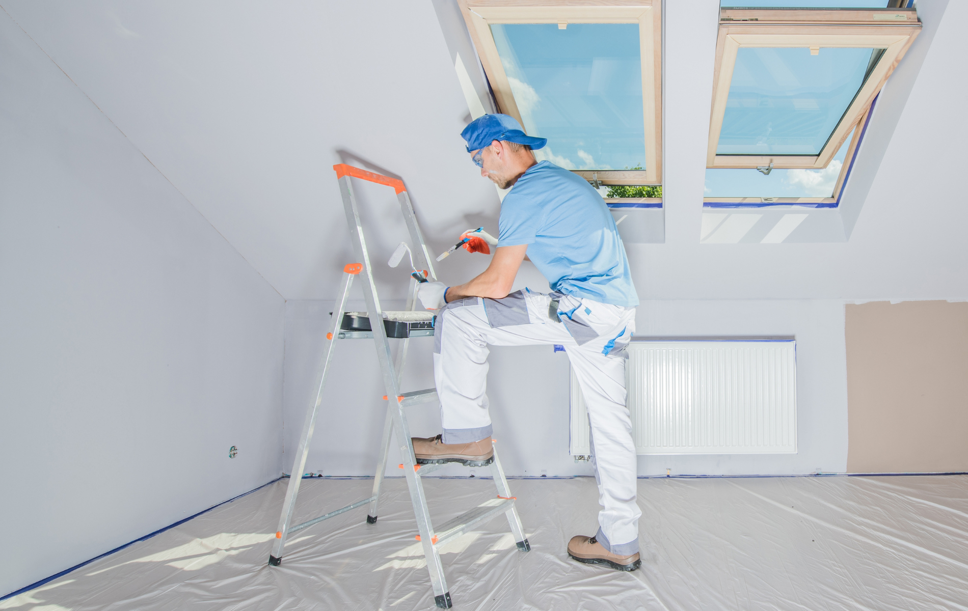 A man is sitting on a ladder painting a wall.