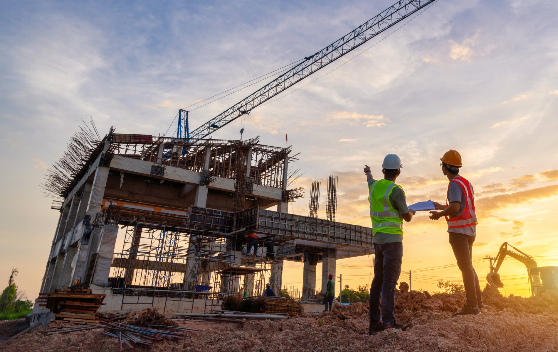 Two construction workers are standing in front of a building under construction.