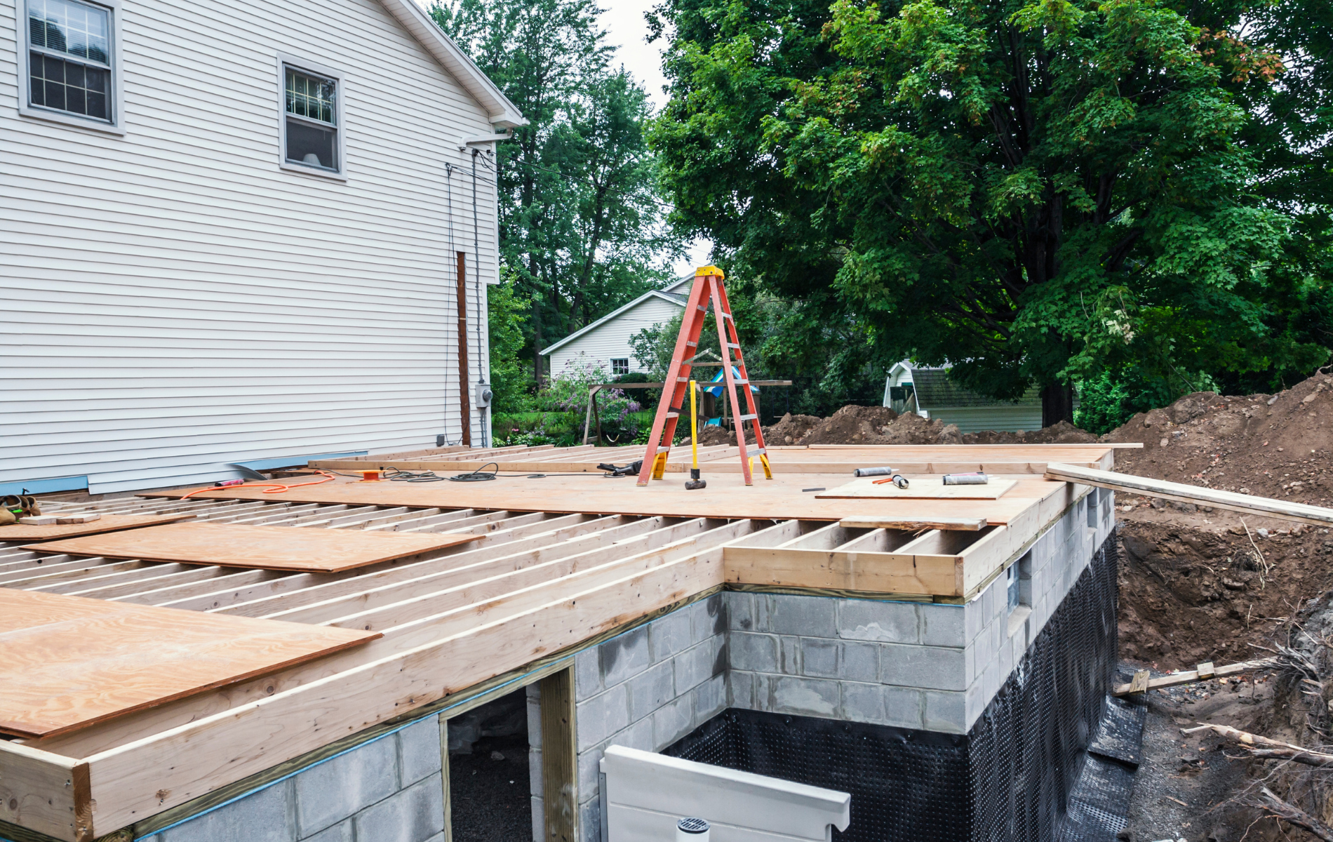 A ladder is sitting on top of a wooden floor in front of a house under construction.
