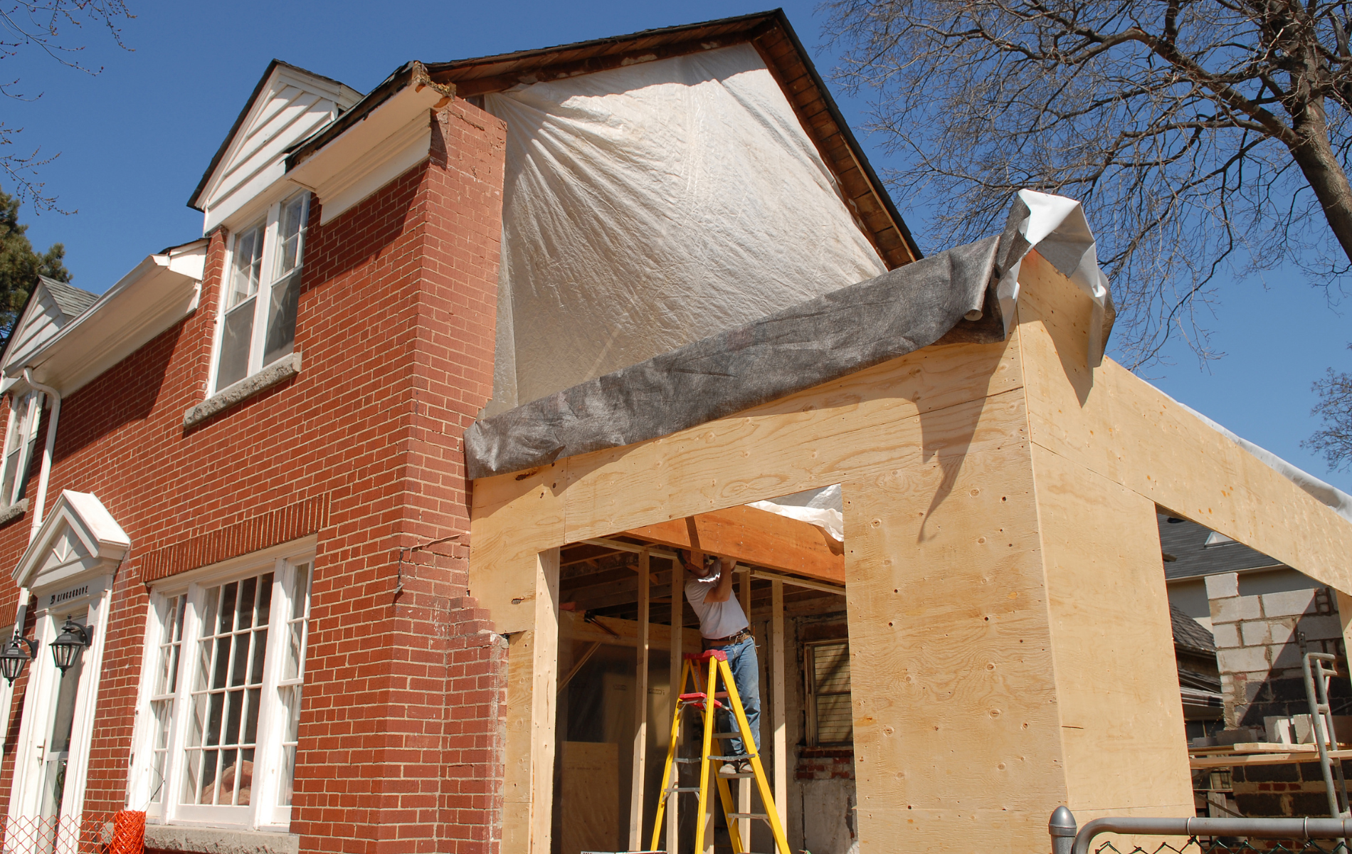A man is standing on a ladder in front of a brick house under construction