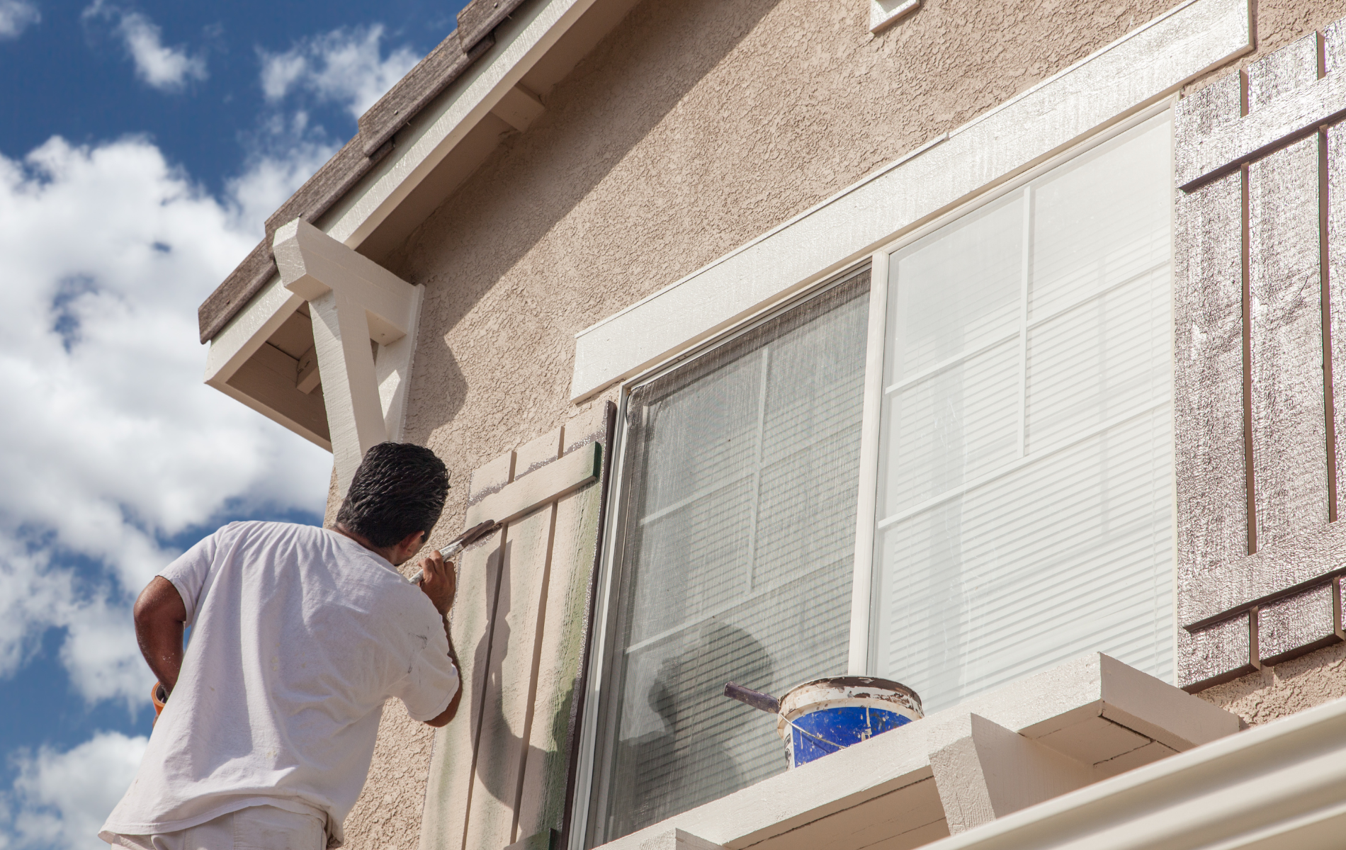 A man is painting a window on the side of a house.