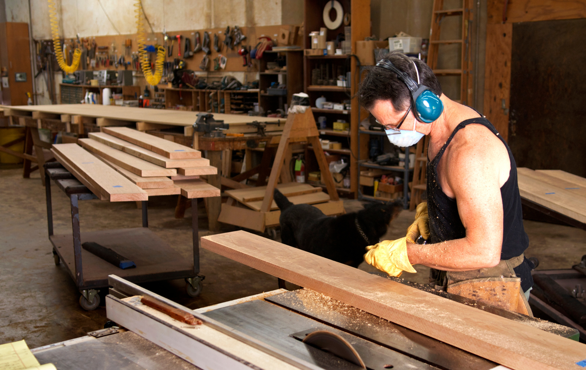 A man wearing a mask is cutting a piece of wood on a table saw.