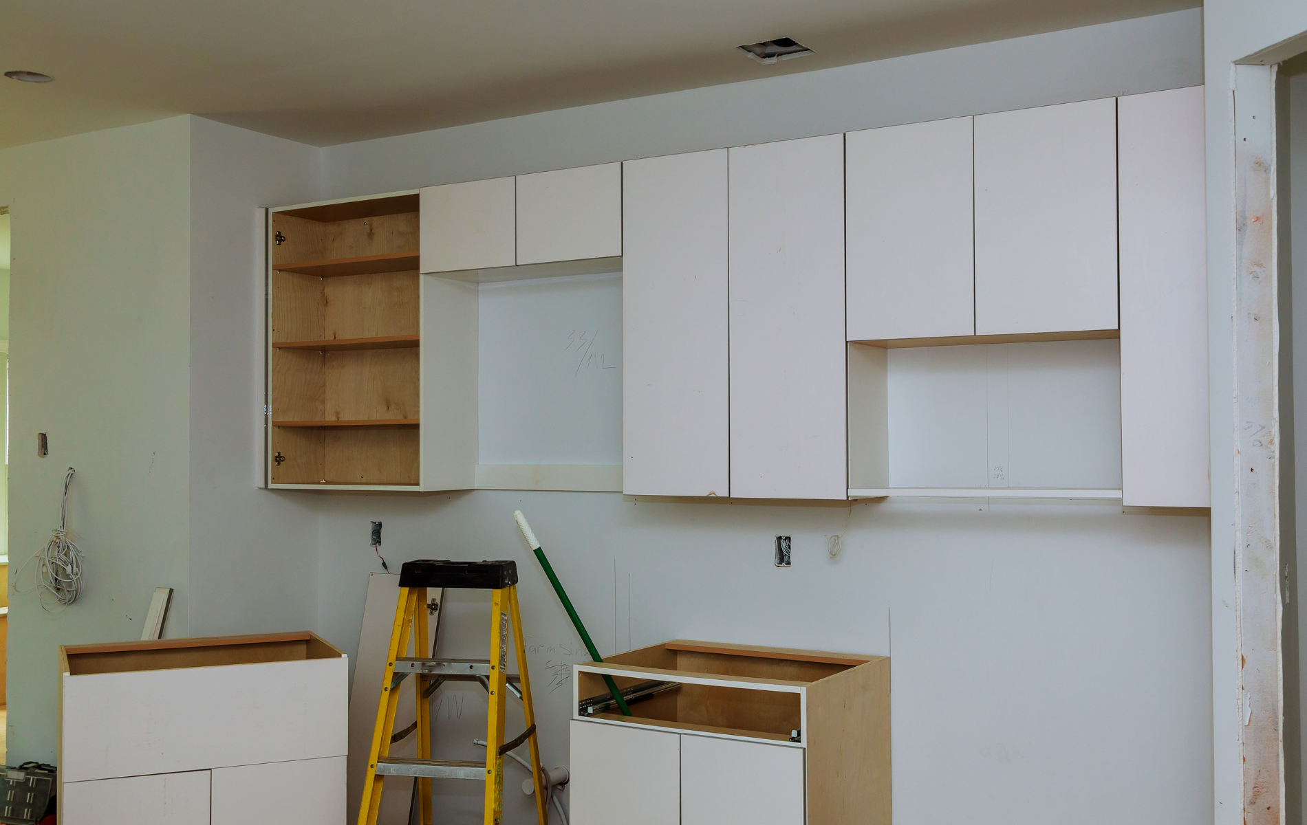 A kitchen is being remodeled with white cabinets and a yellow ladder.