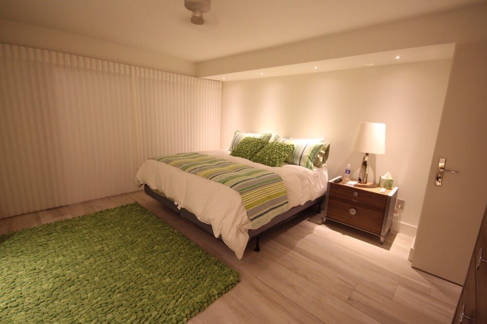 A bedroom with a bed , nightstand , lamp and green rug.