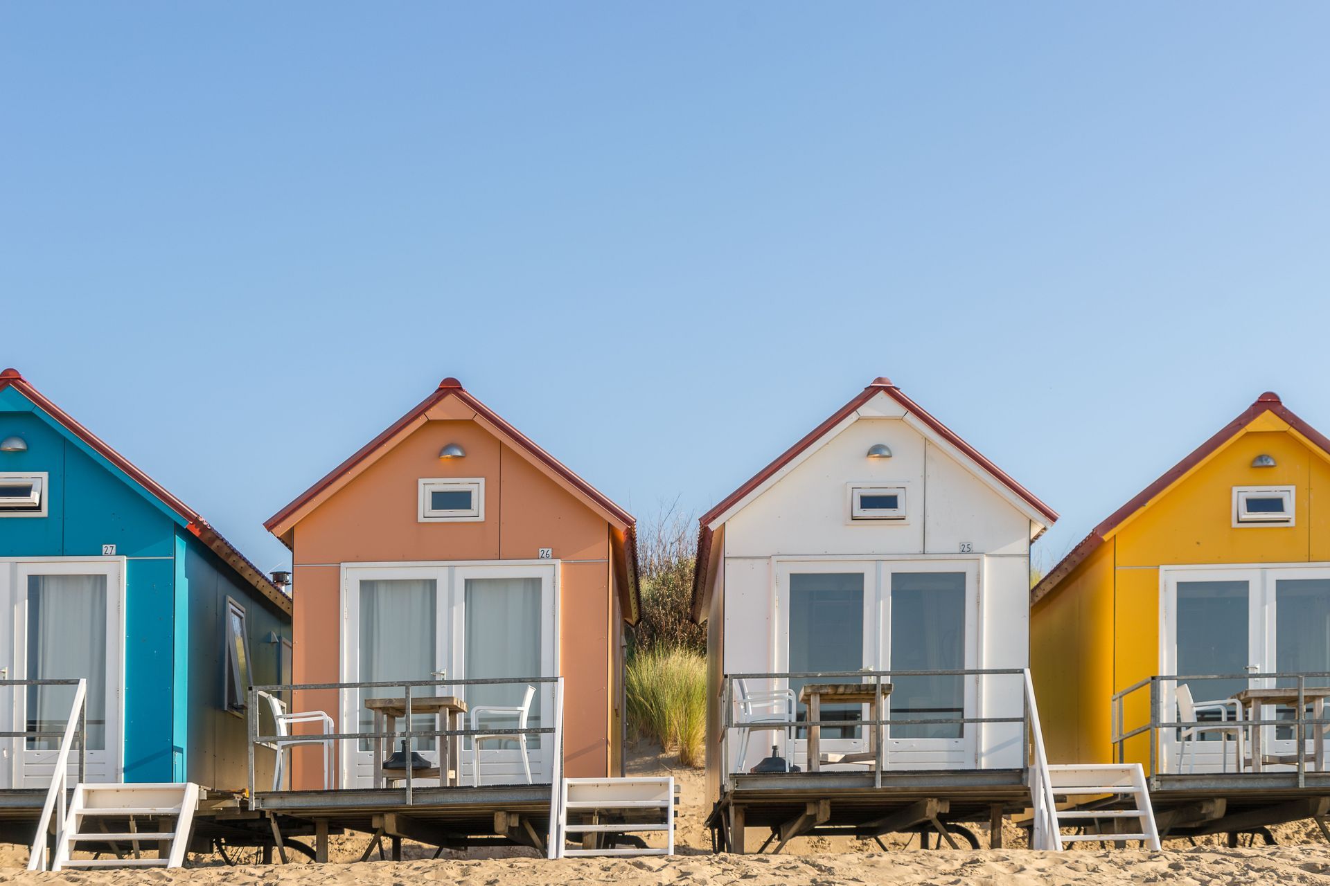 Row of colorful beach cabins on sand under a clear blue sky