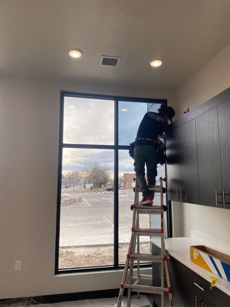 Person installing window film on a building window, standing on a ladder.