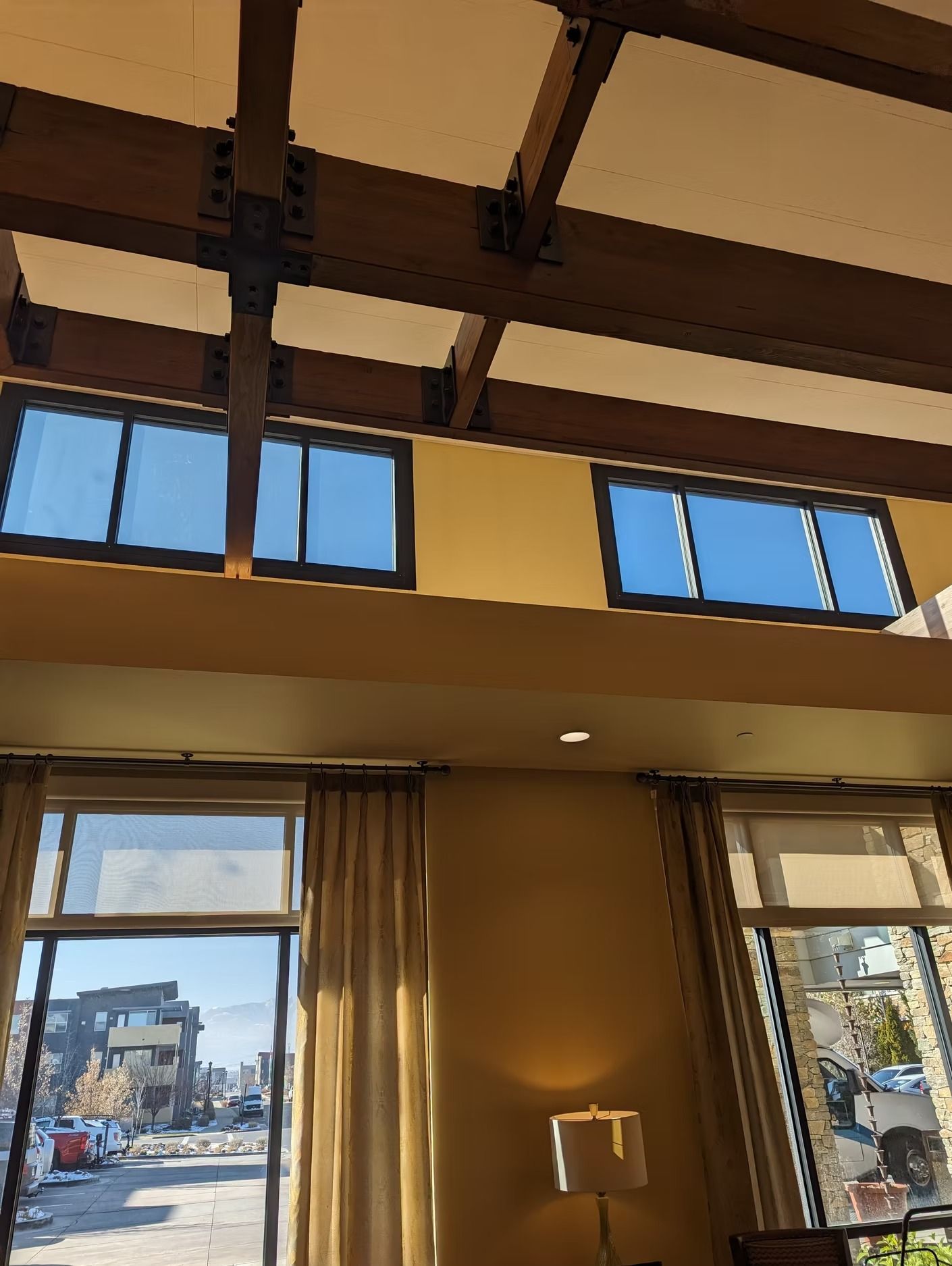 Interior view of a building with large windows, beams, and muted yellow walls.