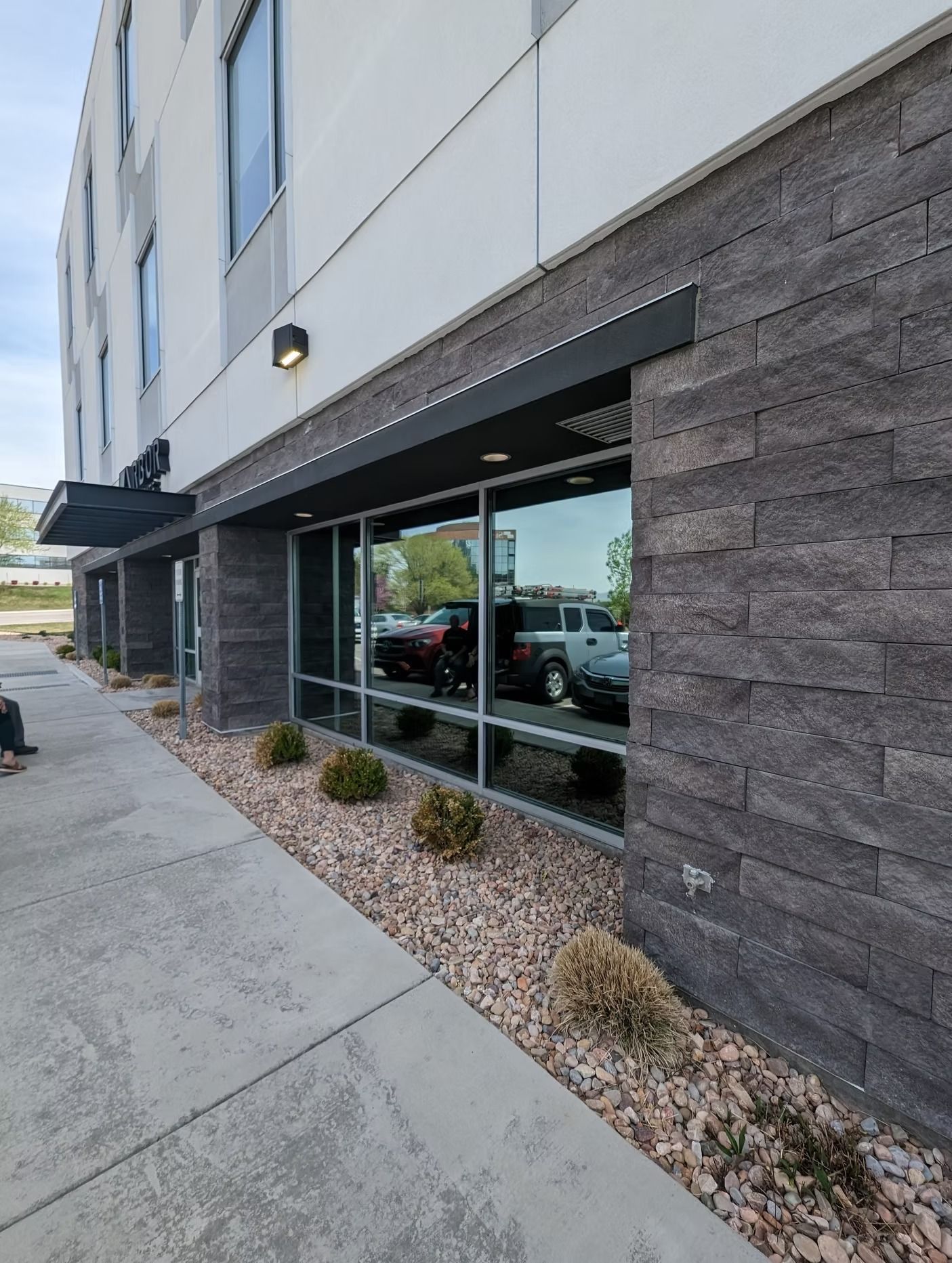 Exterior of a modern building with large windows and stone accents. Sidewalk and landscaping are in front.